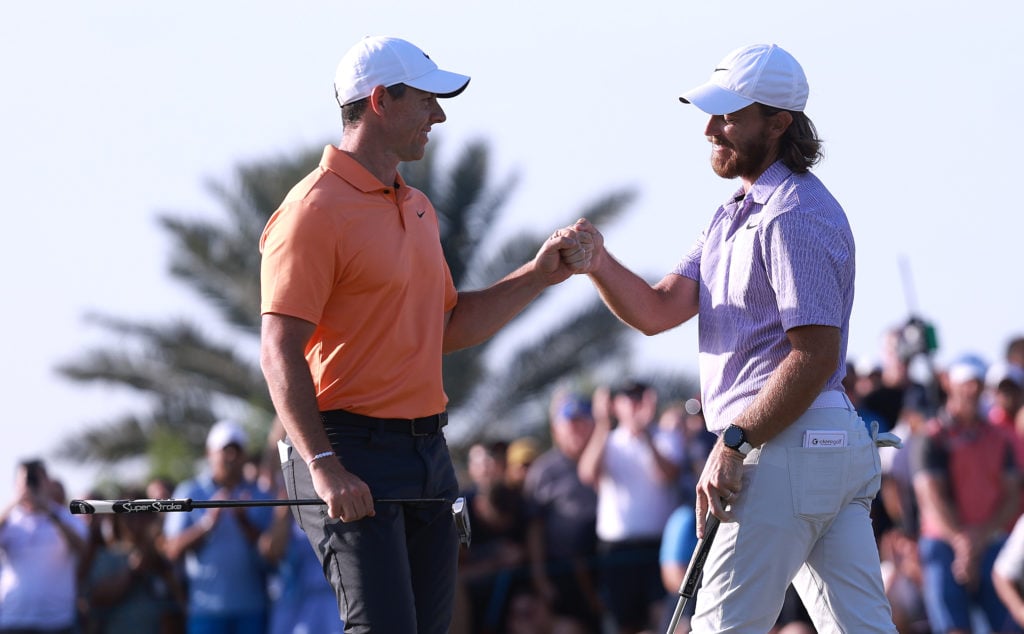 Rory McIlroy of Northern Ireland and Tommy Fleetwood of England bump fists on the 18th green as Fleetwood holes a putt to win the Dubai Invitational