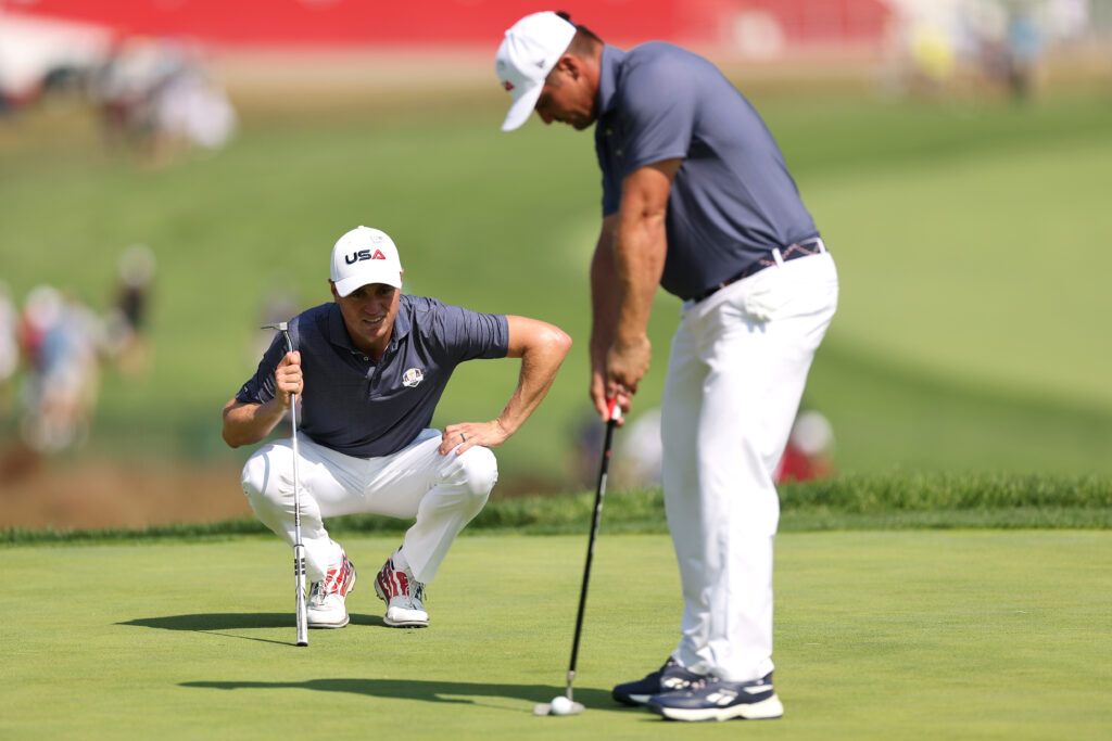 Justin Thomas watches as Bryson DeChambeau hits a putt during a practice session ahead of the Ryder Cup