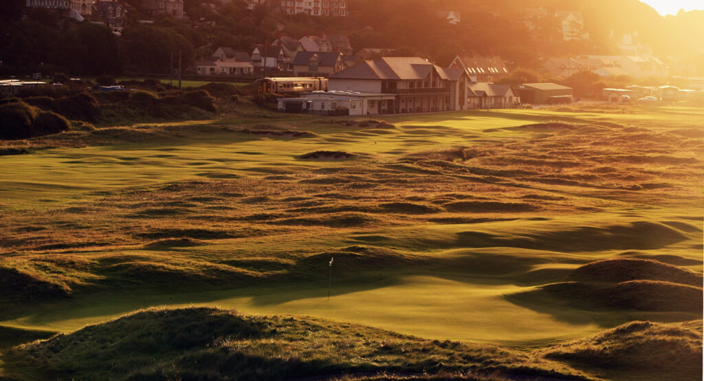 The green on the par 4, 1st hole with the par 4 18th hole and clubhouse behind at The Aberdovey Golf Club