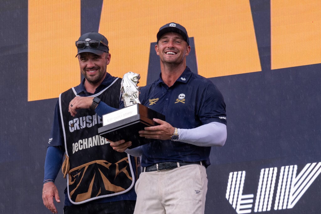 Bryson DeChambeau of Crushers GC holds the trophy alongside his caddie Greg Bodine after winning LIV Golf Singapore at Sentosa Golf Club